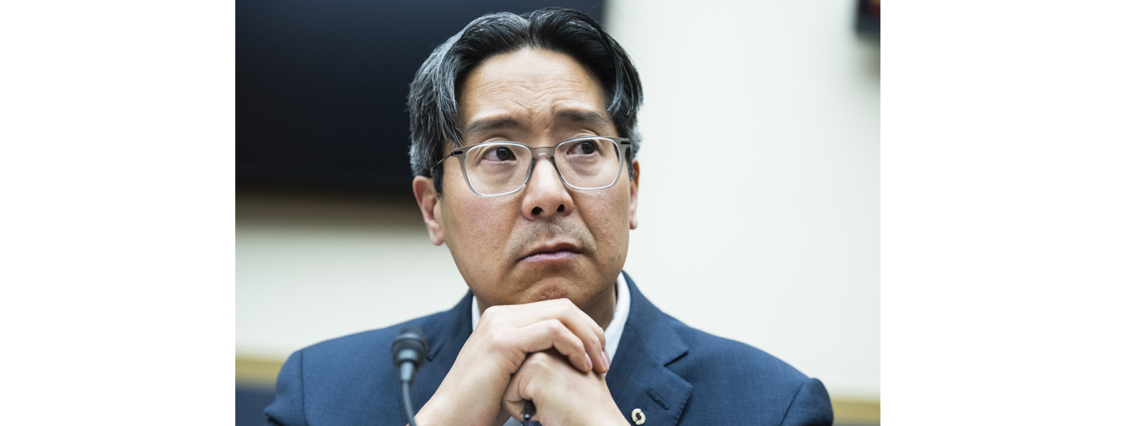 Close-up of Acting Comptroller Hsu during a hearing, with hands clasped and a thoughtful expression.